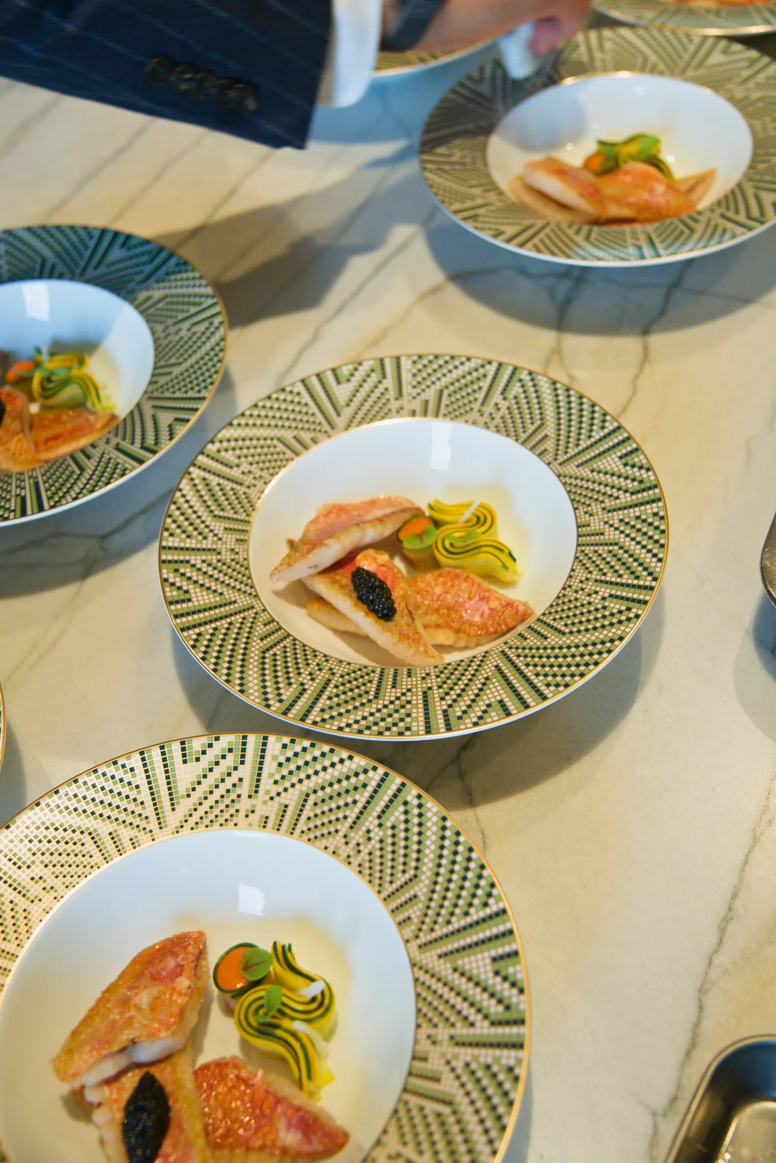 Vue en plongée d'assiettes dressées de filets de rouget au caviar et rubans de courgette