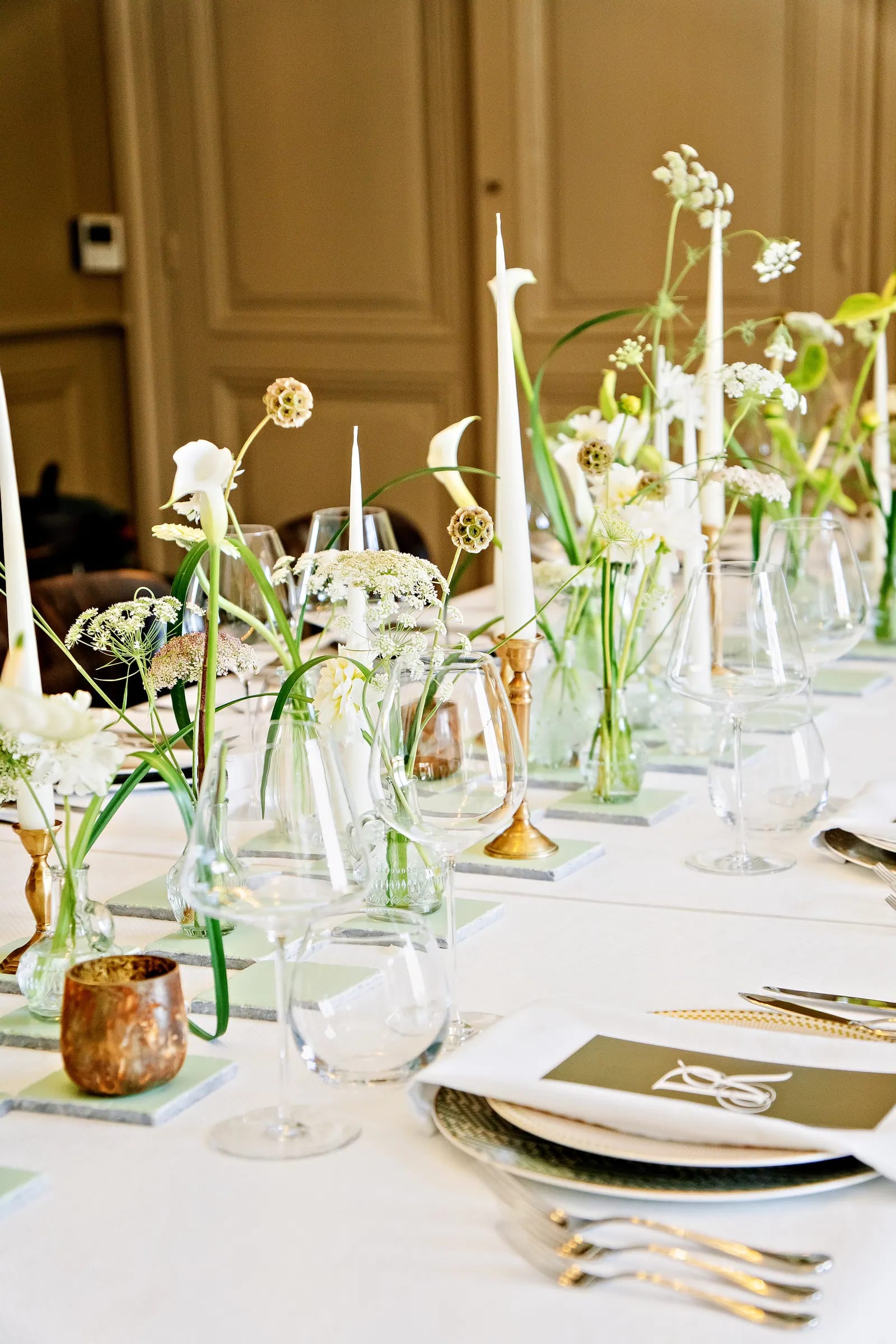 Table dressée avec chemin de fleurs blanches, bougies effilées et bougeoirs en laiton