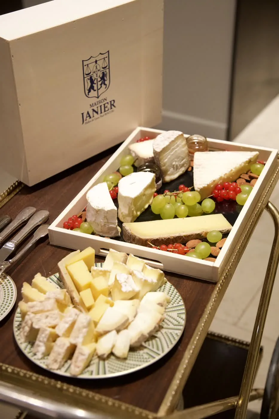 Chariot de fromages affinés Maison Janier — plateau brie, tomme, raisin, groseilles et amandes, servi au guéridon, coffret Maison Janier en fond