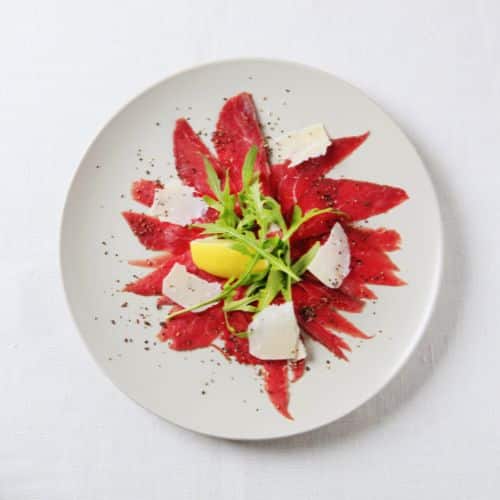Carpaccio de bœuf en rosace, copeaux de parmesan, roquette fraîche et citron – dressage élégant sur assiette blanche