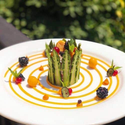 Charlotte d'asperges vertes garnie de fromage frais et fruits rouges, décorée de spirales de coulis exotique et de fruits frais