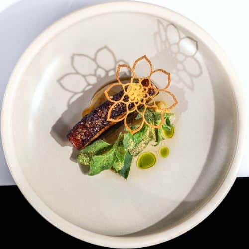 Saumon laqué accompagné d'une tuile florale croustillante, jeunes pousses, et points d’huile d’herbes – dressage raffiné de Chef Sean