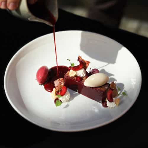 Entremets au chocolat noir et cerise, coulis de fruits rouges versé à la main, quenelles glacées, crème montée et tuiles croustillantes