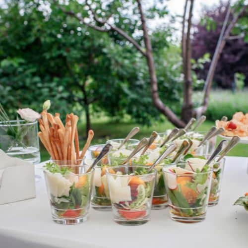 Verrines apéritives fraîches avec légumes croquants, parmesan et gressins pour cocktail gastronomique en plein air.
