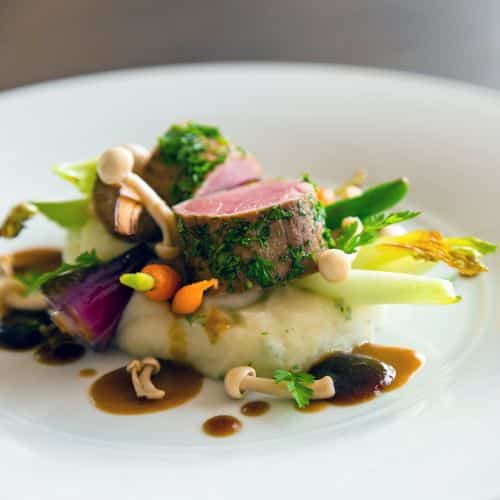 Herb-crusted lamb medallion with mashed potatoes, seasonal vegetables, mushrooms, and jus – fine dining plating.