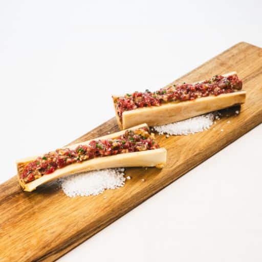 Roasted bone marrow filled with tartare, served on a wooden board with a bed of coarse salt.